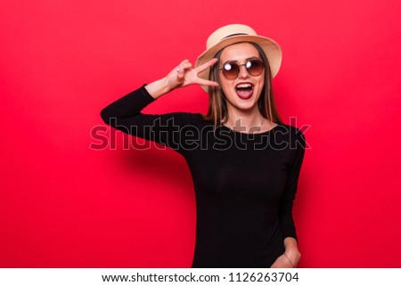 Portrait of gorgeous brunette woman looking at camera with smile and showing peace sign with fingers isolated over red background