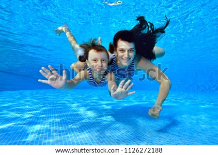 Happy mom and daughter swim underwater in the pool in striped swimsuits, look at the camera and smile. Portrait. Underwater photography. Landscape orientation.
