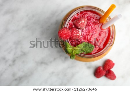 Apricot smoothie with raspberries in a glass jar on a marble background.