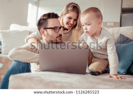 Smiing parents and their little son using laptop at home.