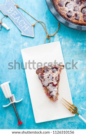 Clafoutis with cherries, cut in slice and put on a cream dish, over a concrete blue background, summertime conceptual food photography.