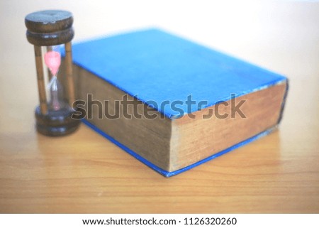 Close-up of old books placed on the table an hourglass beside selective focus and shallow depth of field
