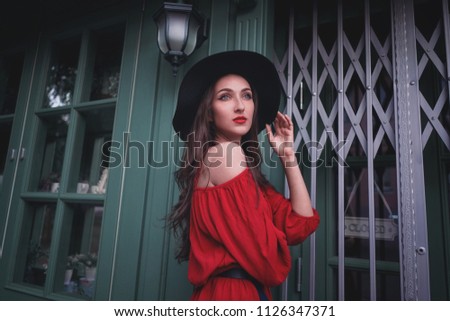 Elegant brunette young woman wearing red dress and straw hat on the street cafe. Fashion and style.