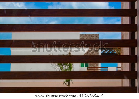 Modern tropical beach house against blue sky viewed through wooden slats