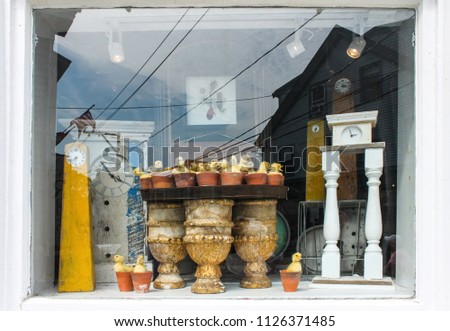 Clocks in a window - Reflections and display of antique clocks and baby ducks in flower pots in Cape Cod window with another clock and American flag and sky reflected