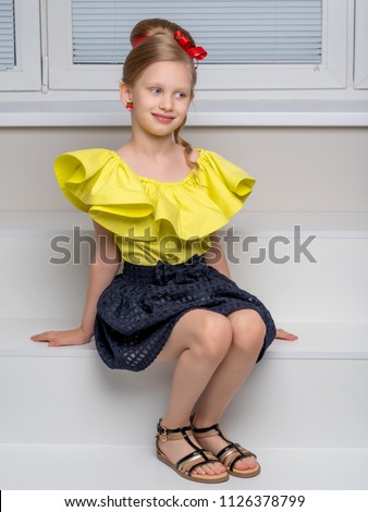 A charming little girl in a smart dress sits on a white staircase. The concept of happiness, childhood.