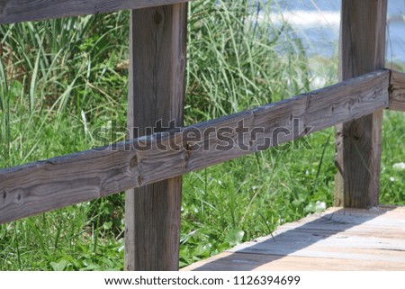 Perspective photography of wood fence railing boardwalk beach access with green plants, turquoise blue water, horizon and sky.