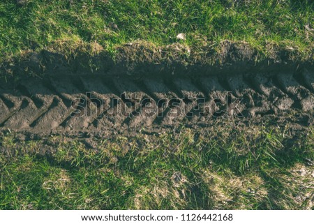 Tractor tire tracks in green grass. mud in spring - vintage retro look