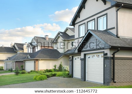 Street with two-storied brown cottages with built-in garage. Green grass near houses. Royalty-Free Stock Photo #112645772