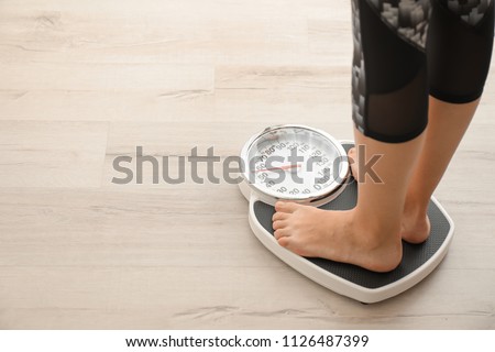 Woman measuring her weight using scales on wooden floor. Healthy diet Royalty-Free Stock Photo #1126487399