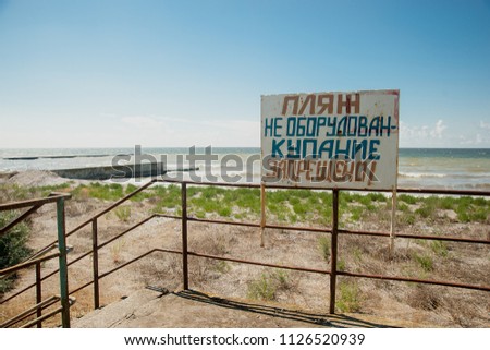 Warning sign on the shore. Text in Russian: the beach is not equipped. swimming is forbidden. Prohibited access to the shore. no swimming. Denied access to water.