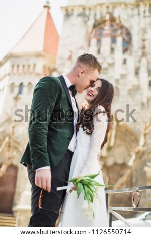 The happy young stylish newlyweds standing in an embrace outdoors