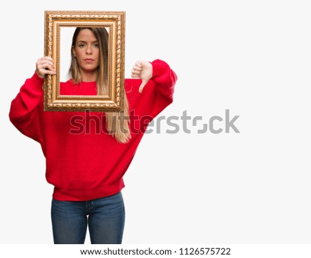 Beautiful young woman holding vintage frame with angry face, negative sign showing dislike with thumbs down, rejection concept