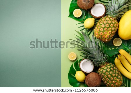 Exotic pineapples, coconuts, banana, melon, lemon, tropical palm and monstera leaves on green, turquoise background with copyspace. Creative layout. Monochrome summer concept. Flat lay, top view