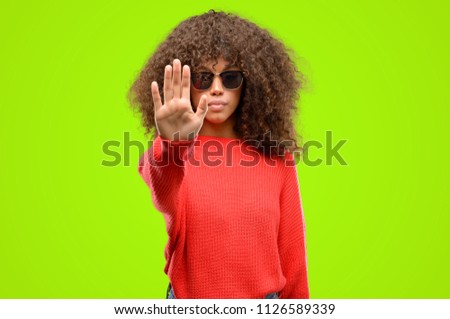 African american woman wearing sunglasses annoyed with bad attitude making stop sign with hand, saying no, expressing security, defense or restriction, maybe pushing
