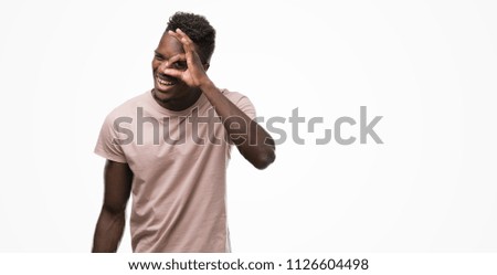 Young african american man with happy face smiling doing ok sign with hand on eye looking through fingers