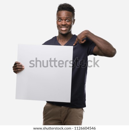 Young african american man holding a banner with surprise face pointing finger to himself