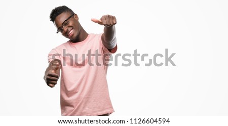 Young african american man wearing pink t-shirt approving doing positive gesture with hand, thumbs up smiling and happy for success. Looking at the camera, winner gesture.