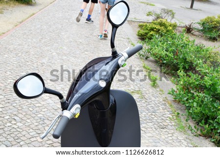 Steering wheel of black electric scooter with mirrors closeup with view of Berlin street on background.
