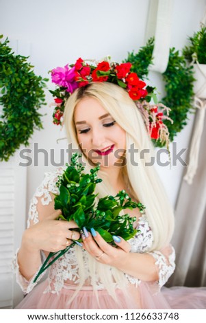 A charming blonde in a wreath holding green leaves in her hand