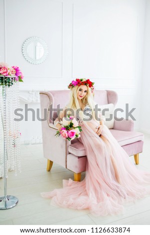 A sweet, pregnant blond woman in a wreath sitting on a sofa