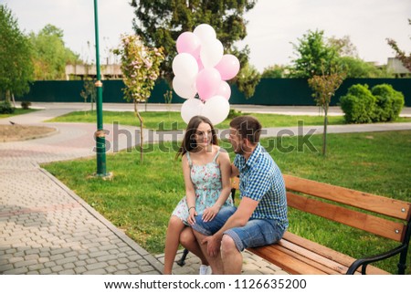 Couple sits on a bench and hold pink helium balls