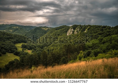 The hilly landscape was suddenly covered by clouds and a heavy rain showered us right after the picture. You can see rocks, valleys, forests and the mountain.