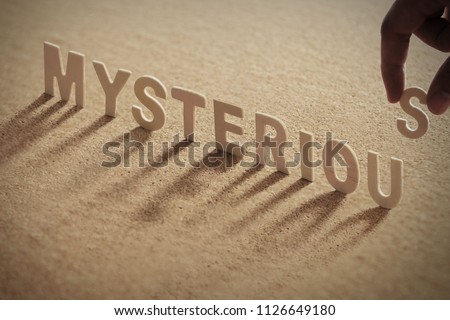 MYSTERIOUS wood word on compressed or corkboard with human's finger at S letter.
