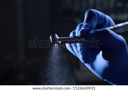 Dentist hand with drill illustrates the operation of the dentist dental drill machine with water. Dentist's hands with blue gloves working with dental drill in dental office. Close up, selective focus Royalty-Free Stock Photo #1126660931