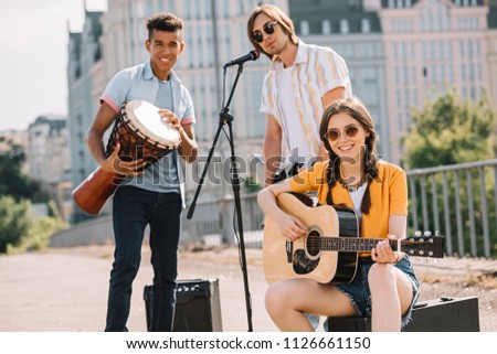 Multiracial young people performing on guitars and djembe on street