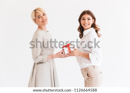 Portrait of beautiful women mother 40s and daughter 16-18 holding gift box together and smiling at camera standing isolated over white background