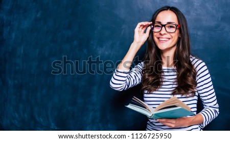 Modern attractive teacher. Portrait of Beautiful smart young woman in glasses with book isolated on the gray background. Study concept