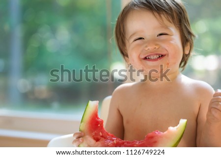 Happy toddler boy eating watermelon in his highchair