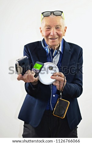 Happy smiling grey haired senior man with modern sunglasses holding and showing old retro devices on white background. Ready to use mockup model concept. Concept of old technology.