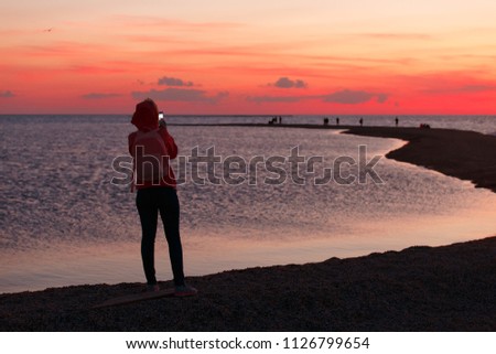 Woman traveler using smartphone and taking photo of colorful sea sunset
