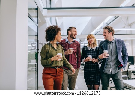 Group of diverse coworkers walking through a corridor in an office, holding paper cups Royalty-Free Stock Photo #1126812173