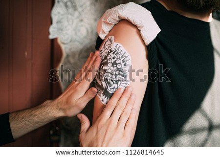 cropped shot of tattoo artist transferring tattoo sketch on shoulder in tattoo salon 