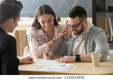 Excited millennial couple signing purchase agreement buying first home together, husband puts signature on document, becoming apartment owner, spouses legalize property ownership in realtor office Royalty-Free Stock Photo #1126819898