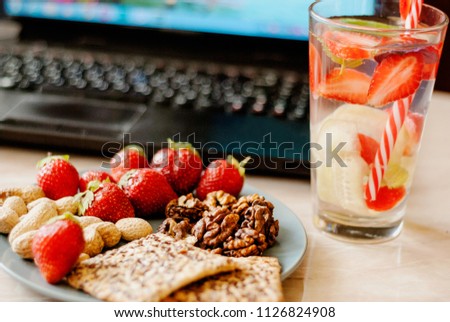 Office employee with laptop, healthy snack, water with strawberry and cucumber. Having strawberries, peanut, walnut, crispbread while working.