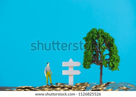 Figure miniature businessman or small people investor standing on coin stack with white wooden board sign and little tree decoration, for money and financial business success concept idea.
