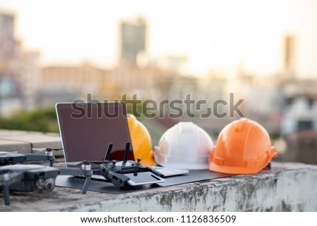 Drone, smartphone, laptop computer and protective helmet at construction site. Using unmanned aerial vehicle (UAV) for land and building site survey in civil engineering project.