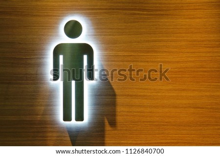 Metal badge of a male toilet with a backlight on a wooden wall