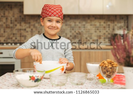 Boy is cooking in a luminous kitchen mixing the preparation while anticipating how tasty it will be with flour oh his face.