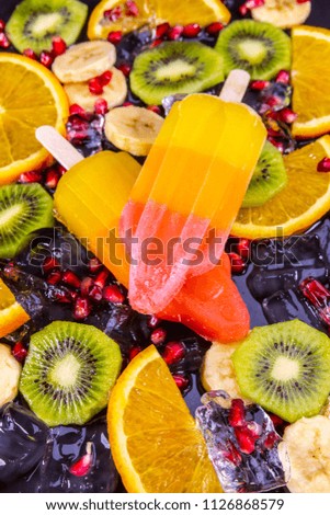 Fruit ice cream on stick with slices fruits on black slate board. Focus on Popsicles.