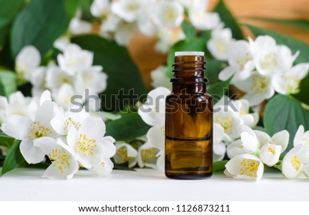 Small bottle of essential jasmine oil. Jasmine blossom flowers background. Copy space. 
