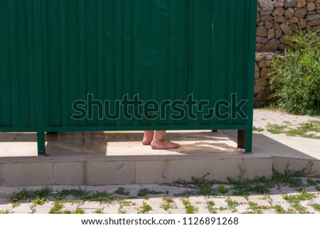 the man's untrodden legs are visible from the dressing room on the beach, the man dresses in a green dressing room made of iron