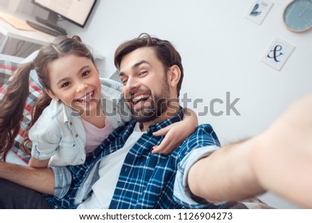 Bearded man and little girl at home family time sitting on sofa hugging taking selfie photos posing smiling cheerful close-up