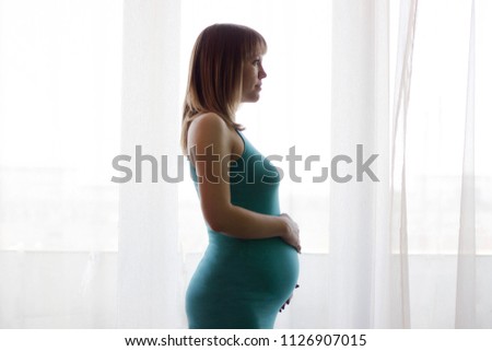 Silhouette of a pregnant girl in a dress in the second trimester opposite the window