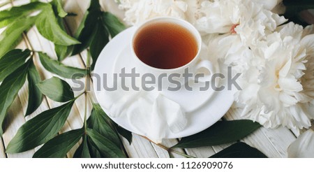 White porcelain cup of green tea and white fresh peonies on light gray wooden background. Top view, concept of relaxation.