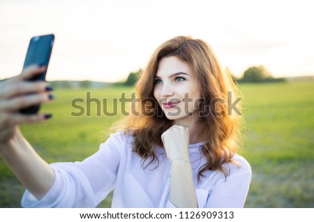 Young blond girl doing selfie on smartphone. against the background of nature. The concept of fashion for shooting on the phone. active lifestyle